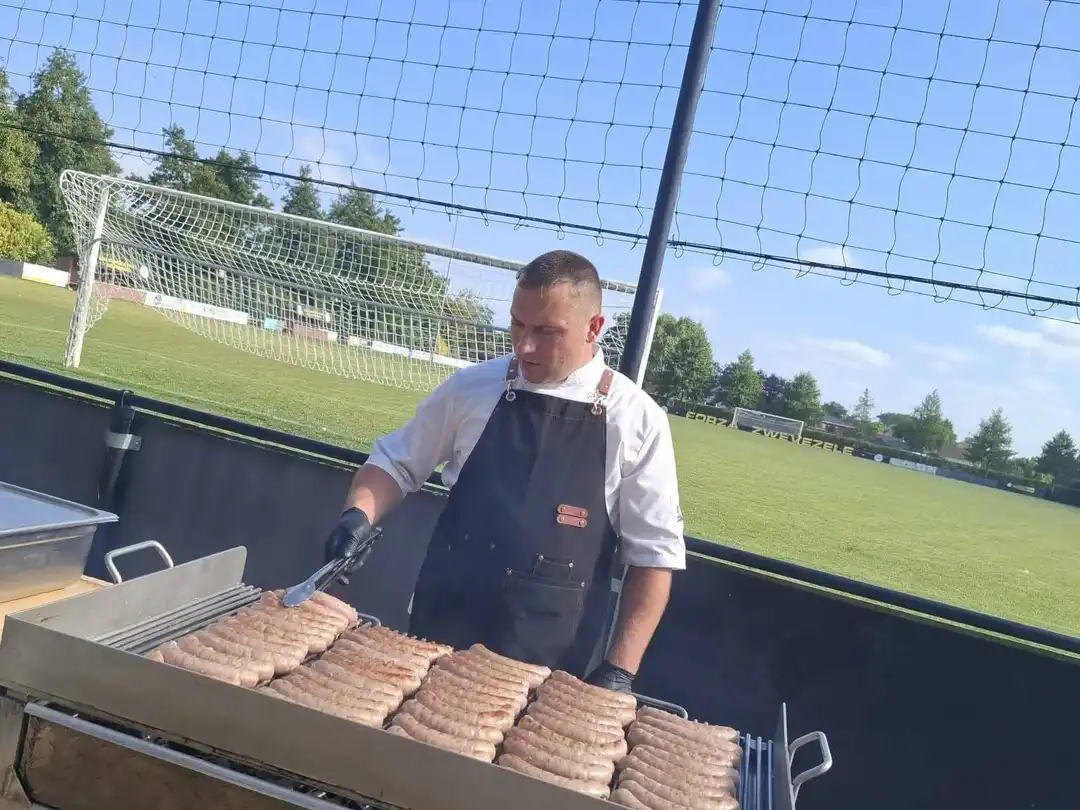 John aan de barbecue met braadworsten, bij een feest buiten