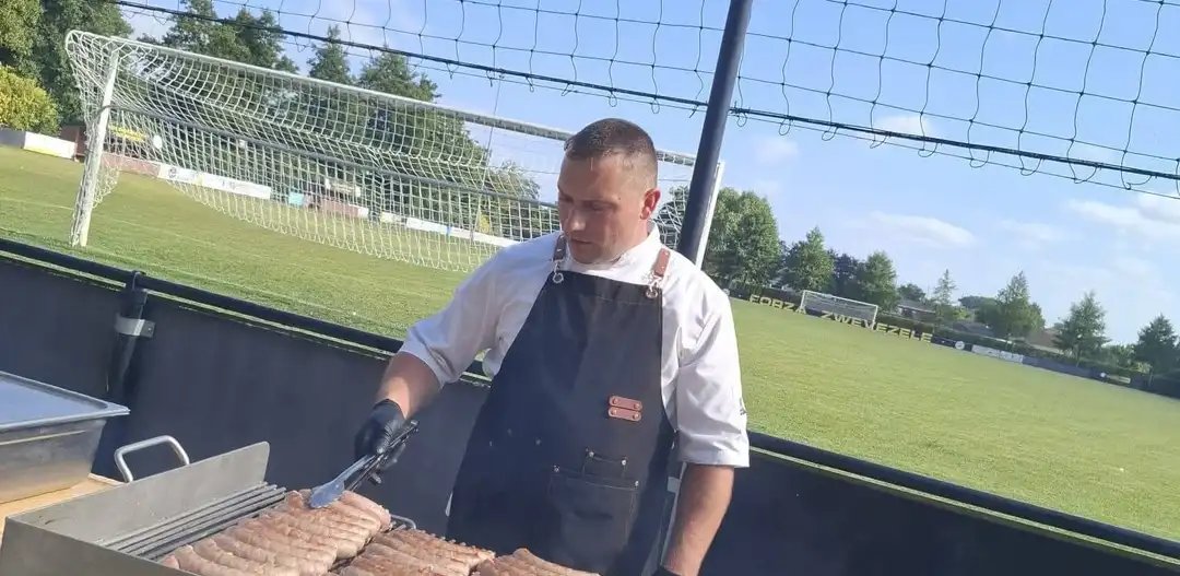 John aan de barbecue met braadworsten, bij een feest buiten