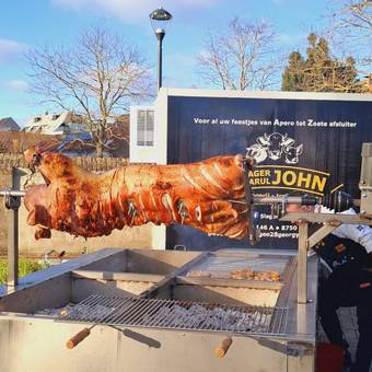 Een varken aan het spit boven de open grill, voor de barbecuetrailer