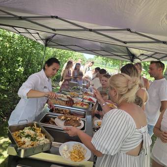 Georgiana schept vlees van de grill op aan een buffet onder een tent, gasten met borden